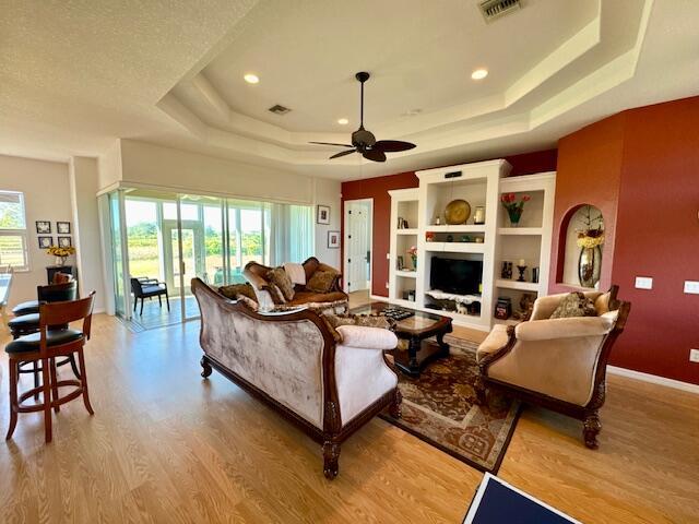 living room featuring ceiling fan, light hardwood / wood-style floors, and a raised ceiling