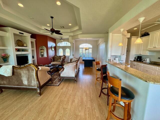 living room featuring a raised ceiling, ceiling fan, sink, and light hardwood / wood-style floors