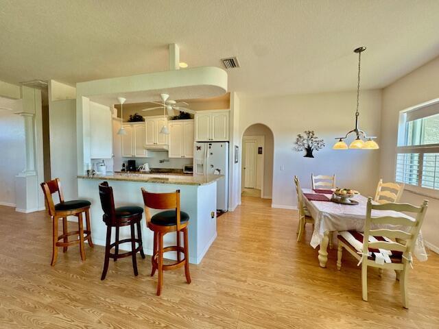 kitchen featuring white refrigerator with ice dispenser, kitchen peninsula, hanging light fixtures, light hardwood / wood-style floors, and white cabinetry