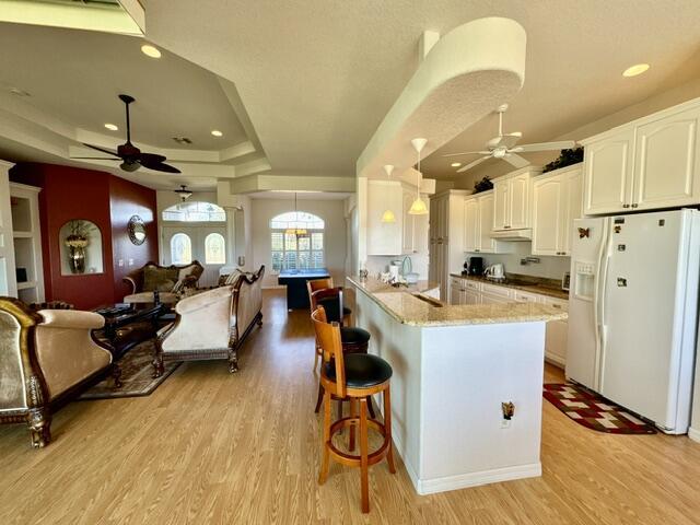 kitchen with white cabinetry, white fridge with ice dispenser, a raised ceiling, kitchen peninsula, and decorative light fixtures