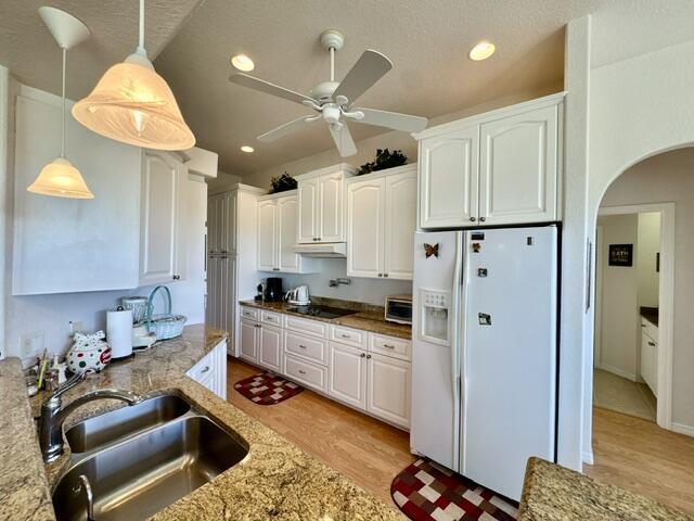 kitchen with white cabinetry, white fridge with ice dispenser, and light stone counters