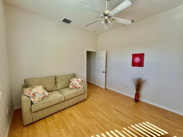 living room with a textured ceiling, light hardwood / wood-style flooring, and ceiling fan