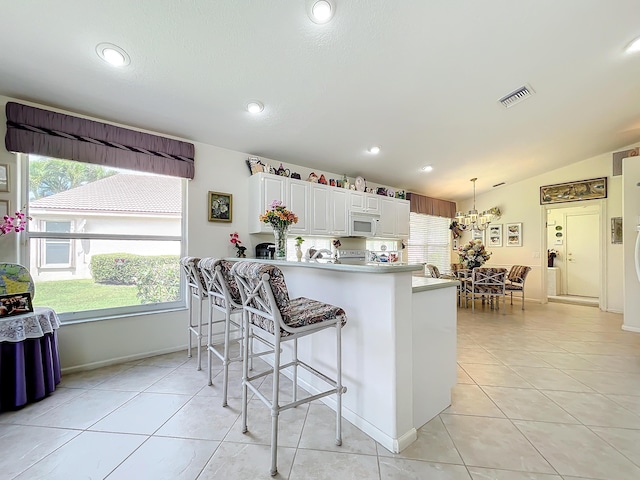 kitchen with hanging light fixtures, white cabinets, kitchen peninsula, vaulted ceiling, and light tile patterned floors