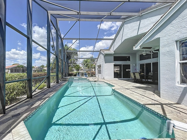 view of swimming pool with glass enclosure, ceiling fan, and a patio