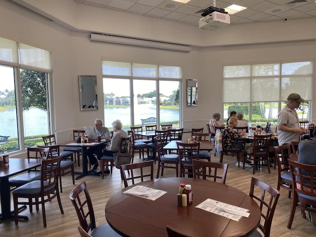 dining space featuring a paneled ceiling, light hardwood / wood-style flooring, and a water view