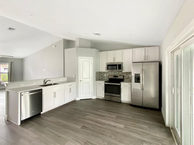 kitchen featuring kitchen peninsula, tasteful backsplash, stainless steel appliances, sink, and white cabinetry