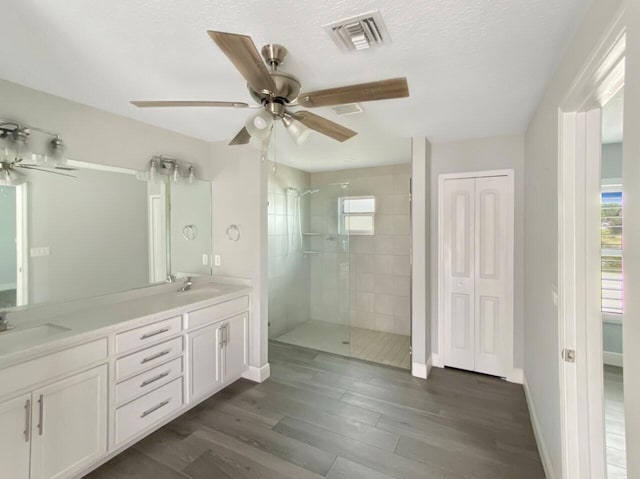 bathroom featuring vanity, a textured ceiling, ceiling fan, tiled shower, and wood-type flooring