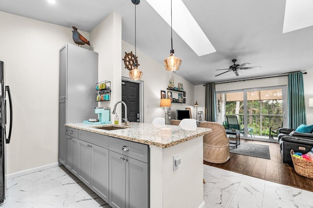 kitchen featuring sink, gray cabinets, hanging light fixtures, light stone countertops, and kitchen peninsula