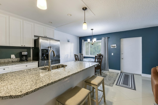 kitchen featuring sink, hanging light fixtures, stainless steel refrigerator with ice dispenser, a breakfast bar area, and white cabinets