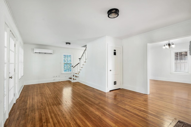 unfurnished living room featuring an AC wall unit, hardwood / wood-style floors, ornamental molding, and a notable chandelier