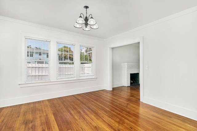 unfurnished dining area featuring ornamental molding, a fireplace, a chandelier, and hardwood / wood-style flooring