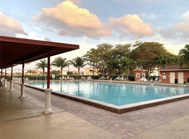 pool at dusk with an outdoor structure and a patio