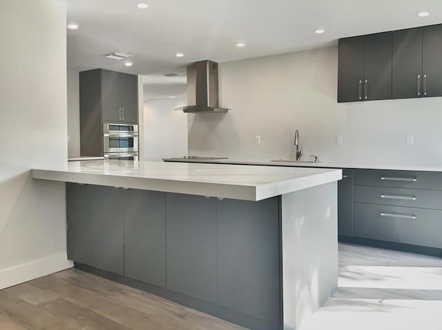 kitchen featuring kitchen peninsula, gray cabinets, wall chimney range hood, and sink