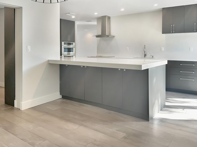 kitchen featuring gray cabinetry, wall chimney exhaust hood, and kitchen peninsula