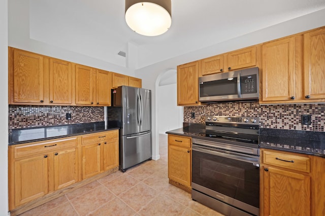 kitchen featuring decorative backsplash, appliances with stainless steel finishes, light tile patterned floors, and dark stone counters