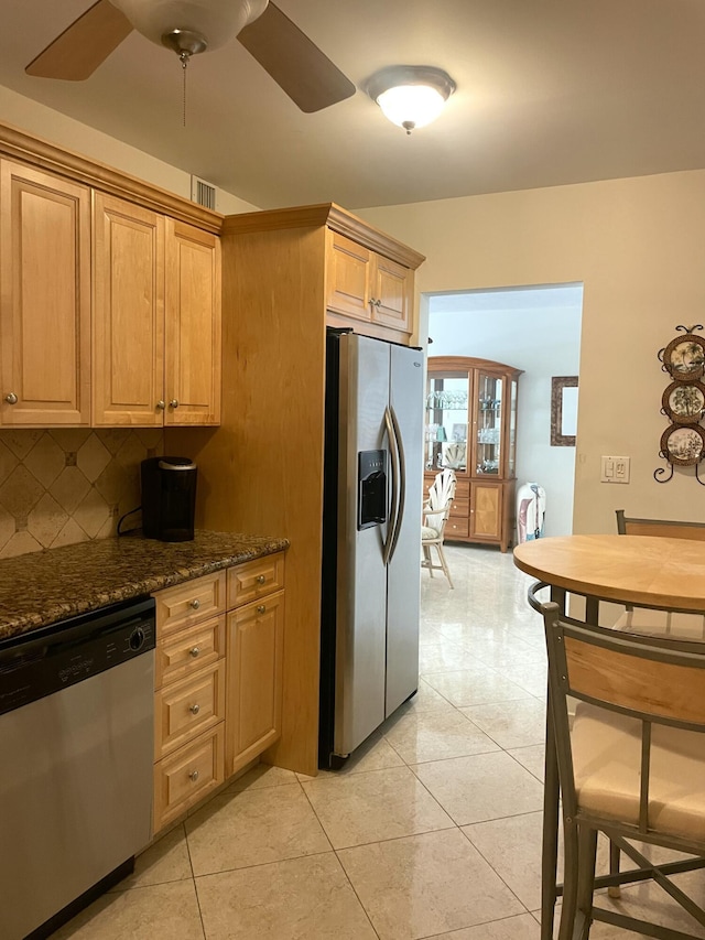 kitchen featuring ceiling fan, backsplash, dark stone countertops, light tile patterned flooring, and appliances with stainless steel finishes