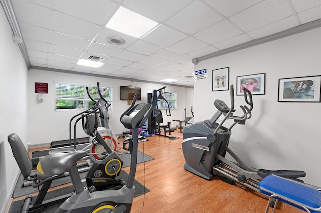 gym with wood-type flooring, a paneled ceiling, and crown molding