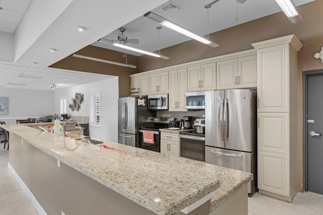 kitchen featuring ceiling fan, sink, a large island, stainless steel appliances, and light stone counters