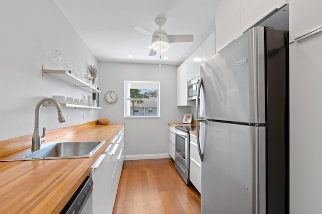 kitchen featuring light wood-type flooring, stainless steel appliances, ceiling fan, sink, and white cabinets