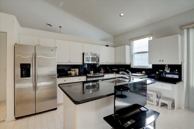 kitchen with a textured ceiling, stainless steel appliances, a kitchen island with sink, sink, and white cabinets