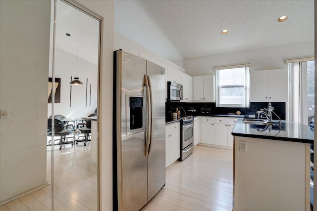 kitchen with appliances with stainless steel finishes, backsplash, sink, white cabinetry, and hanging light fixtures