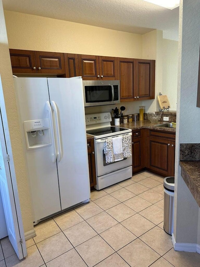 kitchen with light tile patterned floors, white appliances, a textured ceiling, and sink