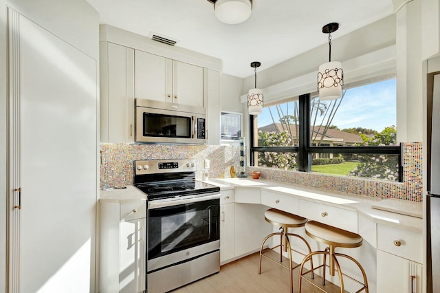 kitchen with appliances with stainless steel finishes, backsplash, light wood-type flooring, decorative light fixtures, and white cabinets