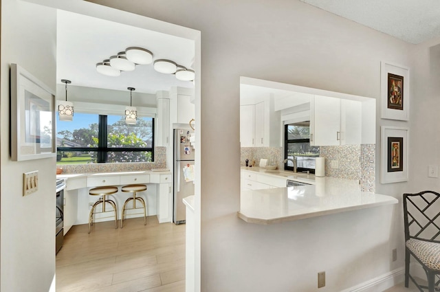 kitchen featuring kitchen peninsula, tasteful backsplash, stainless steel appliances, white cabinets, and hanging light fixtures