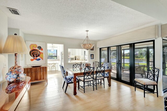 dining area with french doors, a textured ceiling, and light hardwood / wood-style flooring