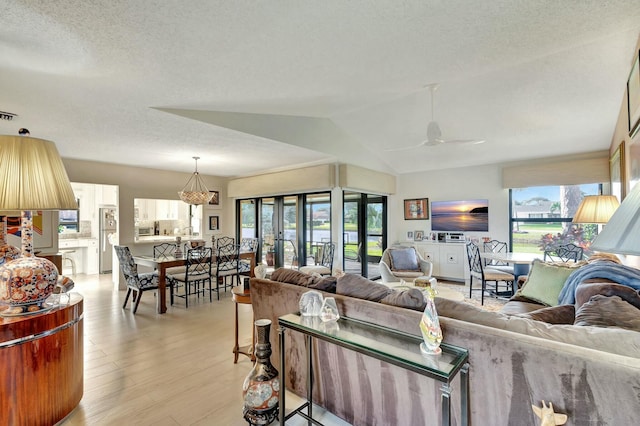 living room with a textured ceiling, light hardwood / wood-style floors, vaulted ceiling, and ceiling fan