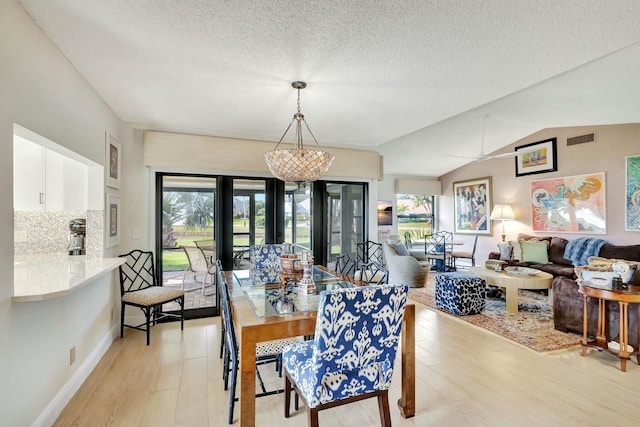 dining room featuring a textured ceiling, vaulted ceiling, light hardwood / wood-style flooring, and an inviting chandelier