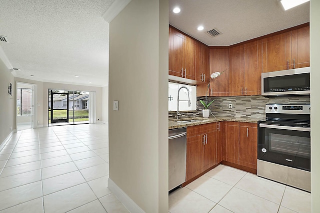 kitchen with appliances with stainless steel finishes, sink, backsplash, light tile patterned floors, and light stone counters