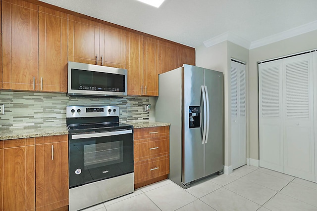 kitchen featuring appliances with stainless steel finishes, tasteful backsplash, ornamental molding, light tile patterned floors, and light stone countertops