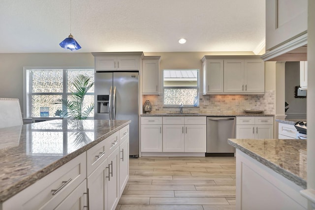 kitchen with pendant lighting, light stone countertops, sink, and appliances with stainless steel finishes