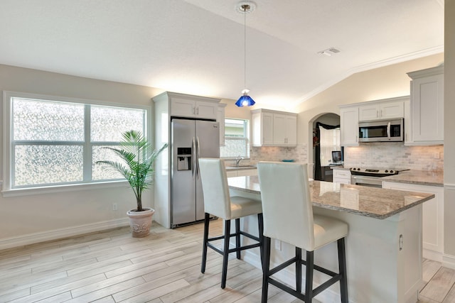 kitchen with light stone countertops, stainless steel appliances, vaulted ceiling, decorative light fixtures, and a center island