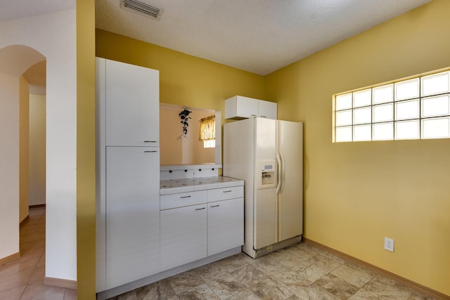 kitchen with white cabinetry, white refrigerator with ice dispenser, and a textured ceiling