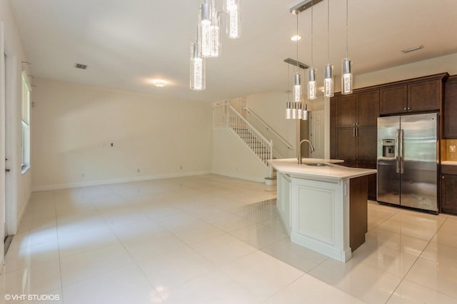 kitchen featuring stainless steel refrigerator with ice dispenser, light countertops, decorative light fixtures, a sink, and dark brown cabinets