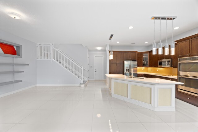 kitchen with decorative light fixtures, stainless steel appliances, light tile patterned floors, and a center island with sink