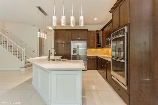 kitchen featuring a sink, stainless steel appliances, light tile patterned floors, an island with sink, and hanging light fixtures