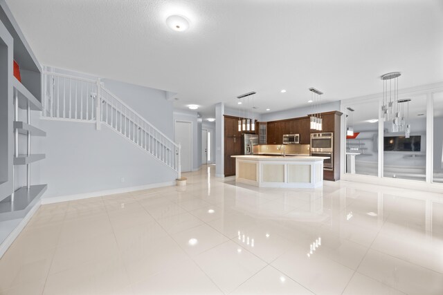 kitchen with stainless steel appliances, sink, light tile patterned floors, a center island with sink, and hanging light fixtures