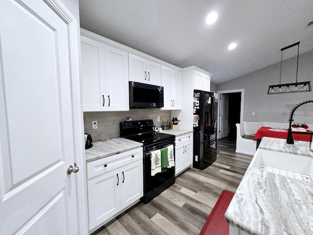 kitchen with tasteful backsplash, vaulted ceiling, black appliances, hardwood / wood-style flooring, and white cabinetry