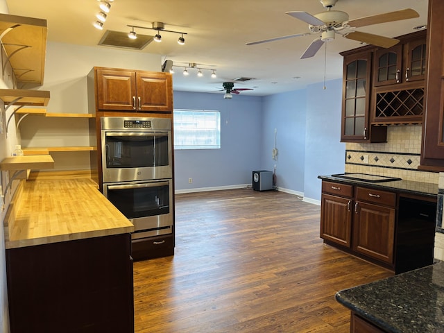 kitchen featuring ceiling fan, dark wood-type flooring, stainless steel double oven, wood counters, and backsplash