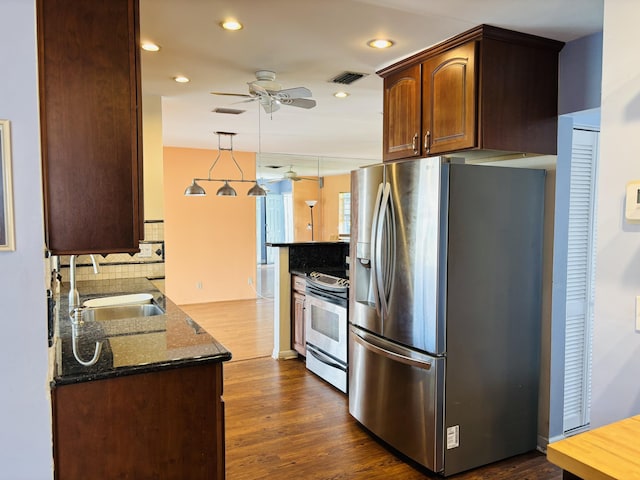 kitchen with sink, hanging light fixtures, dark hardwood / wood-style floors, dark stone countertops, and appliances with stainless steel finishes