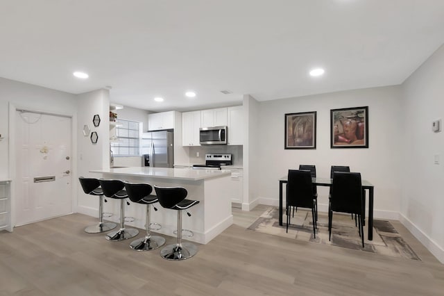 kitchen with a kitchen bar, appliances with stainless steel finishes, backsplash, light hardwood / wood-style flooring, and white cabinets