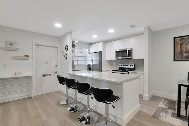 kitchen with a breakfast bar, white cabinets, light hardwood / wood-style flooring, appliances with stainless steel finishes, and tasteful backsplash