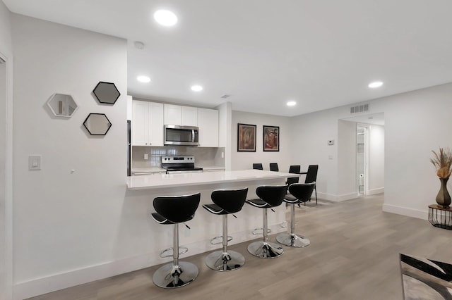 kitchen featuring stainless steel appliances, backsplash, kitchen peninsula, a breakfast bar, and white cabinets