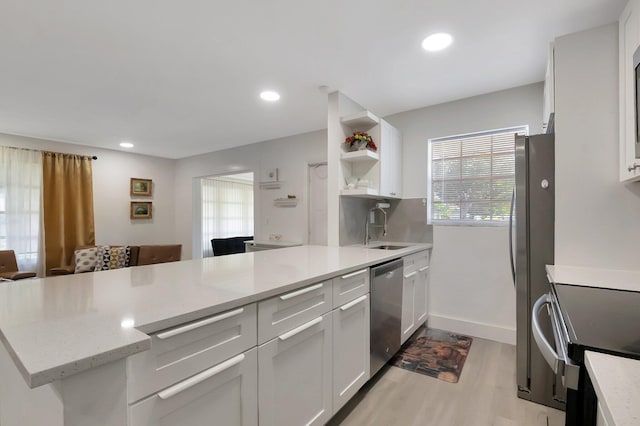 kitchen featuring white cabinets, sink, light wood-type flooring, appliances with stainless steel finishes, and kitchen peninsula