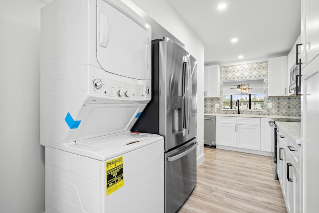 laundry area with stacked washer / drying machine, light wood-type flooring, and sink