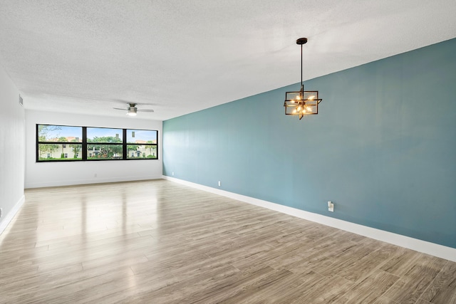 empty room featuring a textured ceiling, ceiling fan with notable chandelier, light hardwood / wood-style floors, and lofted ceiling