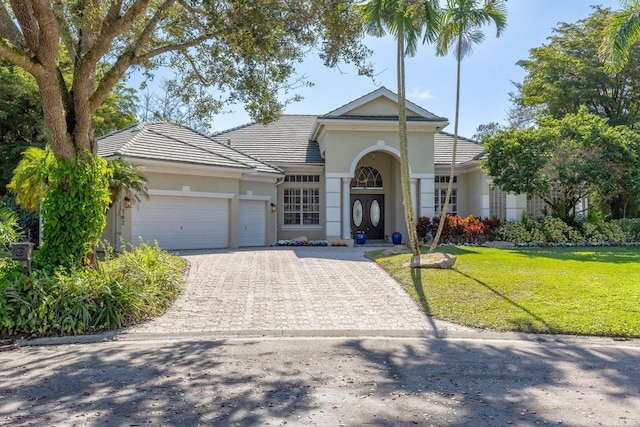 view of front of house with a garage, a tiled roof, decorative driveway, stucco siding, and a front lawn